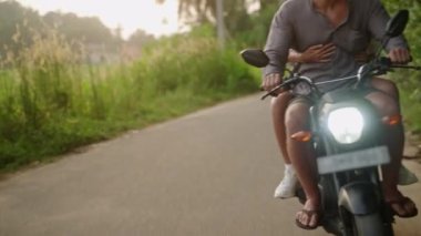 Motosiklete binen mutlu adam ve kadın. Genç aile gün batımında tropik bölgelerde motosikletle seyahat eder. Aşk partnerleri, orman caddesinde scooter kullanır. Güzel turistler egzotik bir adada bisiklet yolculuğunun tadını çıkarırlar..