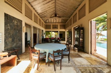 Köy mobilyaları olan klasik bir tropikal villa. Açık uzay yemeği, yuvarlak masa. Sıcak güneş ışığı, sıcak atmosfer. Palmiye ağaçları, havuz kenarında görünür. İnzivaya çekilmek ve tatil yapmak için mükemmel..