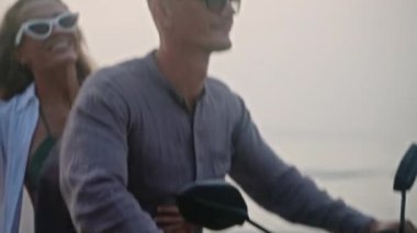 Seyahat eden çiftler gün doğumunda deniz sahilinde motosiklet sürerler. Bisikletten insana aktarma kurulumu. Turistler okyanus kıyısında kiralık motosiklet kullanıyorlar. Kadınlar erkeklere sarılır, motosiklet sürerek kollarını açar..