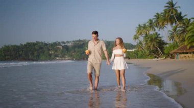 Mutlu çift okyanus sahilinde yürür, hindistan cevizi suyu içer. Genç kadın, erkek el ele tutuşur, gezintide öpüşür. Romantik yeni evliler kokteyl içer, gün doğumunda tropikal deniz kıyısında balayı tatilinin tadını çıkarırlar..