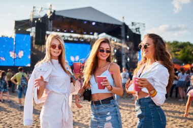 Gülümseyen kadın katılımcılar kutlama yapıyor, deniz kenarında sosyalleşiyorlar. Bir grup genç kadın kumlu plajda yaz müzik festivalinin keyfini çıkarıyorlar, içkiler, güneşli bir günde kalabalığın arasında dans ediyorlar, sahne arkasında da sahne var..