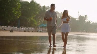 Neşeli çift deniz sörfünün kenarında hindistan cevizi kokteyli içiyor. Gençler gün batımında okyanus kıyısında el ele tutuşmaktan bahseder. Aşıklar tropik adada romantik bir gezide eğleniyorlar..