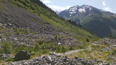 Svaneti dağlarında yürüyüş yapan kadının hava görüntüsü. Engebeli kayalık arazide yalnız kadın yürüyüşçü, yeşil ormanlar, karlı zirveler. Macera, aktif yaşam tarzı, doğa keşfi yaz aylarında doğa yürüyüşü.