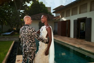 Belirsiz cinsiyet değişkeni beyaz elbiseli siyah gelin ve kalın takım elbiseli LGBTQ damat tropikal villada evleniyor. Eşcinsel-dostu etkinlik için düğün yeri. Çeşitliliği kutlamak, aşk birliği.