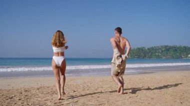 Genç bir adam ve bir kadın elbiselerini çıkarıp okyanusa fırlatıyorlar. Formda bir çift, yaz tatilinde tropikal kumsalda eğleniyor. Aşıklar romantik yolculuktan hoşlanır. Yavaş çekim.