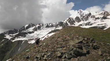 Sırt çantalı, yüksek dağlara tırmanan tek kişilik dağcı görüntüsü. Maceracı bulutlu gökyüzünün altında kayalık araziye çıkar. Açık hava sporu, ekstrem arazi, karlı zirveler doğa keşfi. İHA atışı