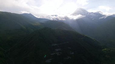 Kazbegi Tepesi 'nin havadan görünüşü, Kafkasya Dağları' ndaki Gergeti Trinity Kilisesi. Manzaralı dağ manzarası, tarihi mekan, yeşil tepeler. Macera arayanlar, yürüyüşçüler, kültür turistleri için doğa merkezi.