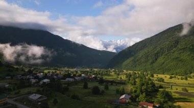 Güneş doğarken Mazeri köyünün görkemli Svaneti dağlarıyla hava manzarası. Yeşil vadi, dağınık evler dingin bulutlar. Çarpıcı barışçıl kırsal alan. Sabahın erken saatlerinde. İHA atışı