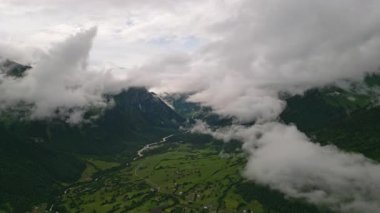 Mazeri köyündeki Svaneti dağlarındaki bulutların üzerinden drone görüntüsü. Zengin yeşillik, dolambaçlı nehir, bulutlu gökyüzü, manzaralı manzara. Seyahat, doğa, hava manzarası dağ keşfi için mükemmel..