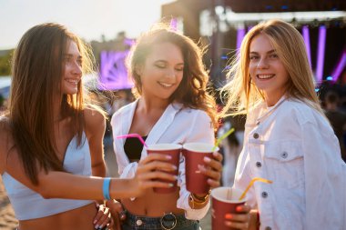 Yaz festivalinde arkadaşlar kadeh kaldırır. Bir grup gülümseyen kadın gün batımındaki plaj partisinde soğuk içeceklerin tadını çıkarıyor. Heyecanlı bayanlar dansı, güneşli okyanus arkaplanı. Boş zaman, eğlence, kıyı müzik etkinliğinde kızlar hafta sonu..