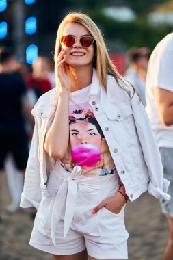 2019-08-10 - Mariupol Şehir Festivali 2019, Ukrayna. Şık güneş gözlüklü gülümseyen kadın plajda yaz müzik festivalinden, pembe balonlu sakızlardan ve günbatımından zevk alır..