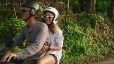Motosikletle seyahat eden neşeli genç bir çift. İki neşeli aşık orman yolunda motosiklet sürüyor. Kız arkadaş gülüyor, kollarını açıyor. Gezginler gün batımında scooter kullanır. Erkek ve kadın macerası.