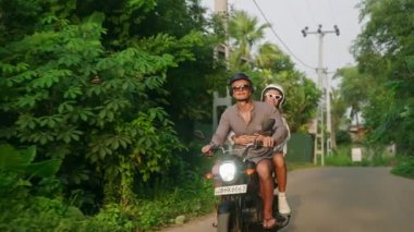 Motosiklete binen mutlu çift. İki sevgili tropiklerde motosikletle seyahat eder. Kız arkadaşı kollarını açar, erkek ormanda scooter kullanır. Gezginler bisikletle yerleri keşfederler. Erkek ve kadın maceradan hoşlanır..