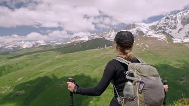 Sırt çantalı gezgin kadın ulusal parktaki dağ manzarasının tadını çıkarıyor. Yürüyüş direkleri ile ayakta duruyor, göz kamaştırıcı manzaranın tadını çıkarıyor. Karlı tepeler, zengin vadiler temiz gökyüzü manzarası. Aktif açık hava macerası.