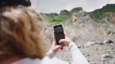 Yürüyüş yapan kadın, dağların fotoğraflarını ve videolarını çeker. Doğayı ve kayalık araziyi akıllı telefonuyla araştırıyor. Açık hava macerası, güneşli bir gün. Seyahat anılarını yakalıyorum. Yavaş çekim.