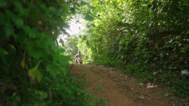 Orman yolunda motosikletle birkaç tur attık. İki kişi toprak yoldan geçiyor, tropik yerlerde bisiklet sürüyor. Dostum, aşık bir kadın motosikletle yolda yuvarlanıyor. Mutlu turistler scooter ile seyahat eder.