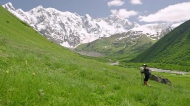 Kadın sırt çantasıyla Jangi-Tau vadisinde Svaneti dağlarına tırmanıyor. Solo kadın yürüyüşçü doğayı keşfeder, arka planda karlı zirveler. Macera, dağcılık, doğa gezisi aktiviteleri.