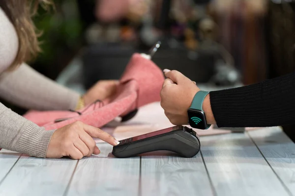 Close-up of a counter with a customer paying with smartwatch contactless system in a clothing shop