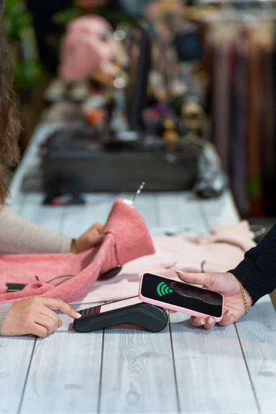 Close-up of a counter with a customer paying with smartphone contactless system in a clothing shop