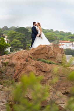 Yeni evli çiftin sahildeki kayalarda öpüşüp kucaklaşmalarının dikey portresi.