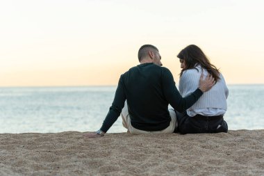 Scene with a man consoling a woman while sitting on the sand at the beach