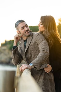 Vertical portrait of a couple in love in a footpath near the beach with the sunset on the background