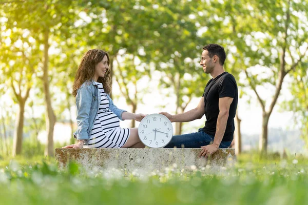 公園に座ってお互いを見ている妊婦と時計と若いカップルとカウントダウンの概念 — ストック写真