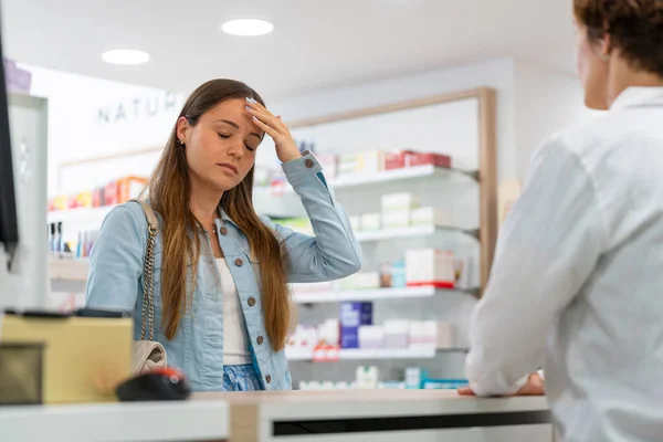 stock image Young woman with a headache expression in a pharmacy talking to a female pharmacist