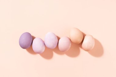 Row of pastel colored Easter eggs on peach background, top view, hard light.