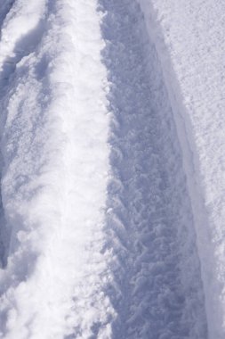 Güneşten parlayan beyaz bir kar yığınının üzerindeki izler, ani bir kar yağışı, yoldaki karlı bir arka planın dokusu, bir araba tekerleğinin izleri, dondurucu bir iklim, dikey olarak