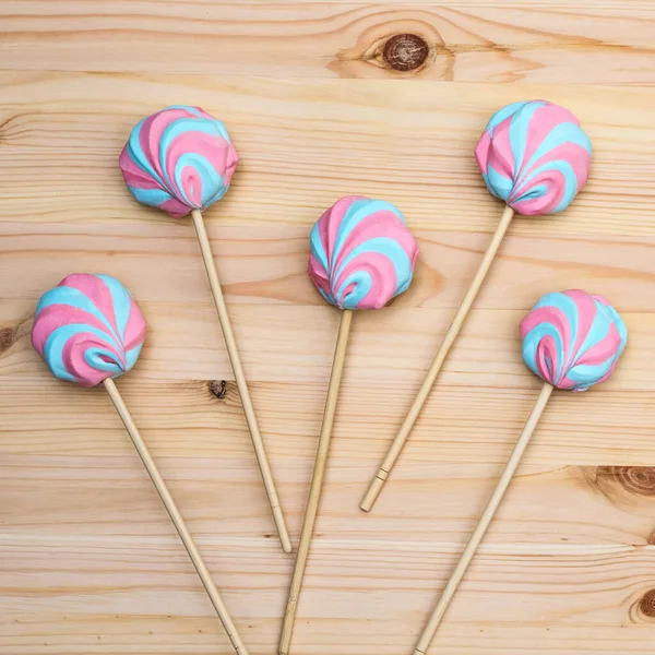 Colorful fluffy marshmallows on sticks on a background of a light wooden surface, close-up, flat lay, top view