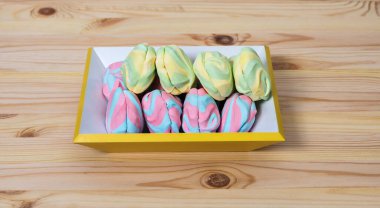 Renkli çizgili kabarık kabarık lokumlar iki sıra halinde açık ahşap bir arka planda sarı bir tabak üzerinde tatlı bağımlılık, baştan çıkarma, yatay, kopyalama, yakın çekim