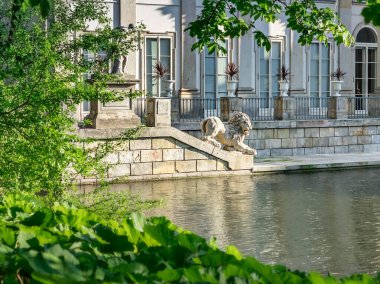 Sudaki saray, üzerinde aslan heykeli olan bir teras parçası. Bir yaz günü ağaç dallarının altından manzarayı seyret. Polonya Varşova 'daki Royal Lazienki Parkı.
