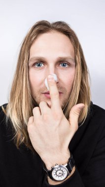 Yakışıklı, uzun saçlı, mavi gözlü ve burnuna bir elin parmağı ile temizleyici köpük süren bir sarışın. Erkekler için kozmetoloji, profesyonel ve ev yapımı cilt bakımı, yakın çekim, dikey...