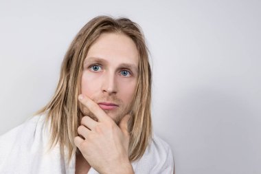 Boynunda ve omuzlarında havluyla yakışıklı, baştan çıkarıcı bir genç adam, tıraş olduktan sonra hassas cildine dokunur. Erkekler için ev bakımı ve kozmetoloji..