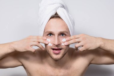 Başında beyaz havluyla ifade eden üstsüz genç bir adam parmaklarıyla yüzüne beyaz krem şeritleri sürüyordu. Yüzünde provokasyon, meydan okuma ve canlı duyguların ifadesi