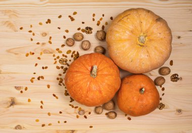 Üç sarı-turuncu balkabağı ve dağınık ceviz ve kuru üzüm ahşap bir masa üzerinde, Cadılar Bayramı konsepti ve sonbahar balkabağı hasadı, tarım ürünü, yatay, üst görünüm, yakın çekim