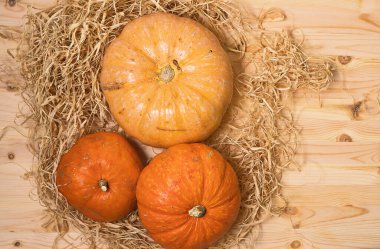 Ahşap bir masa üzerinde samanların arka planında üç sarı-turuncu balkabağı, Cadılar Bayramı konsepti ve sonbahar balkabağı hasadı, bir tarım ürünü, yatay, üst manzara, yakın çekim