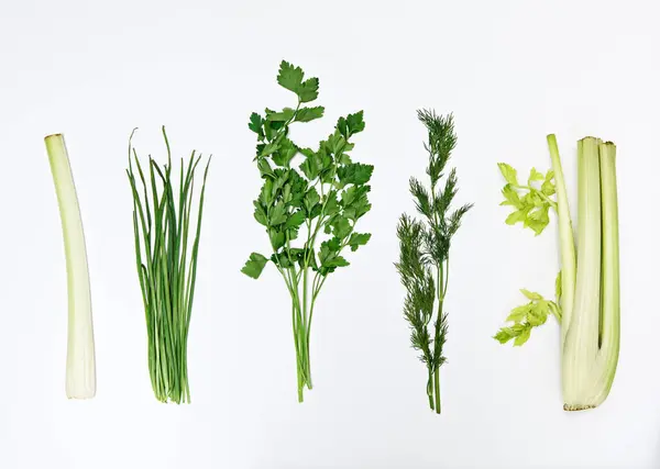 Bunches of green leafy vegetables (parsley, dill, onion) and celery stalks arranged in a row on a white background, isolate.Healthy food concept, fresh garden food diet, organically grown, flat lay