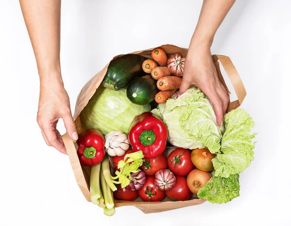 Female hands take a head of Chinese cabbage from a paper bag with various vegetables isolated on a white background. Delivery and purchase of healthy eco food from the supermarket. Top view, horizontal