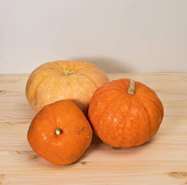 Three yellow-orange pumpkins on a light wooden table, Halloween concept and autumn pumpkin harvest, farm product, horizontal, side view, copyspace