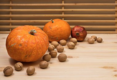 Sarı portakal kabakları, nar meyveleri ve ahşap masaya saçılmış cevizler, Cadılar Bayramı konsepti ve sonbahar balkabağı hasadı, tarım ürünü, yatay, yan görüş