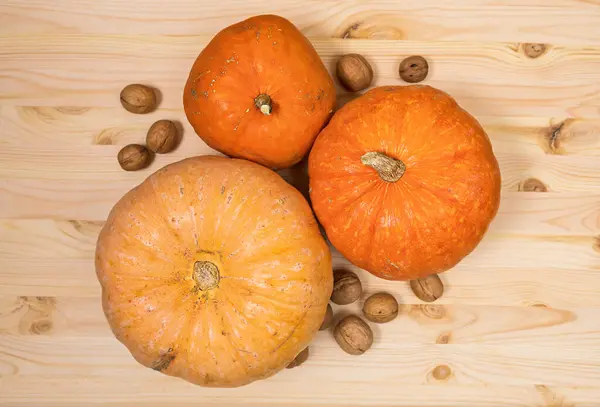 Three yellow-orange pumpkins and scattered walnuts on a wooden table, Halloween concept and autumn harvest of pumpkins, farm product, horizontal, top view, close-up