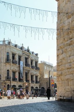 Kudüs, İsrail - 13 Temmuz 2015. Eski Kudüs şehrinde dar bir kaldırım taşı caddesi. Arka planda binalar ve mavi gökyüzü ile caddenin her iki tarafında yürüyen insanlar var.