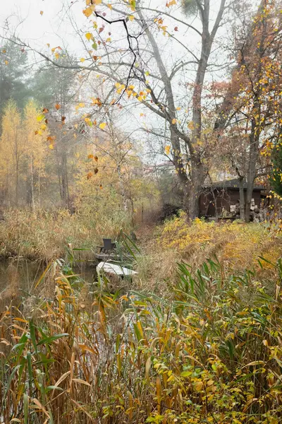 stock image A park bench sits by a pond on a fall day. The trees in the background are turning yellow, orange, and red. The leaves are falling from the trees and floating on the pond.