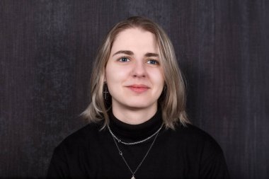 Sıcak bir yüzü, hafif makyajı ve şık bir saç kesimi olan genç bir kadın. Karanlık bir arka plana karşı durarak kendine güveni ve cazibesi yayarak büyüleyici bir görüntü yaratıyor..