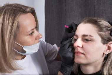 Bir güzellik uzmanının genç bir kadının kaşlarına cımbız sürerek doğal bir görüntü oluşturması.