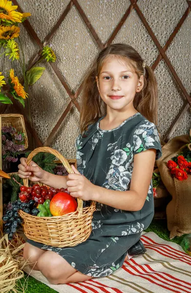 Bir kız neşeli bir şekilde taze meyve ve sebzelerle dolu bir sepetin yanında diz çöker..