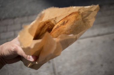 Hand holding cheese bread in a paper bag in morning sun.