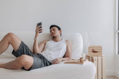 Asian man using mobile phone on his sofa in a relax day off at home. High quality photo